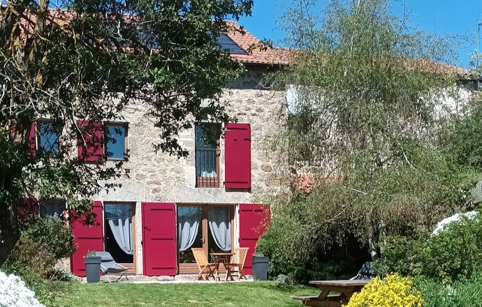 Façade en pierre aux volets rouges et jardin fleuri